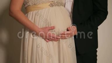 一对夫妇穿着婚纱在怀孕的肚子上的特写。